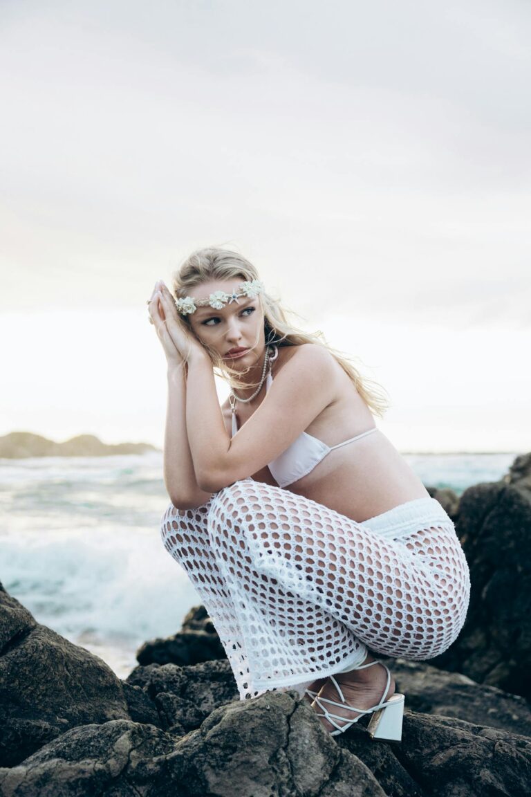 A woman in bohemian attire sitting on rocks by the sea, exuding tranquility.